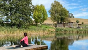 A person sitting on a wooden dock extending over a calm body of water, surrounded by trees and a grassy area. - A Two-storey Home With Terrace and Fireplace - Last Minute (Grossharthau)