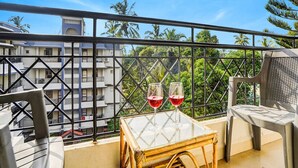 A balcony with a table, two glasses of red wine, and a view of buildings and trees. - Super Townhouse Calangute (Calangute)