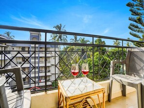 A balcony with a table, two glasses of red wine, and a view of buildings and trees. - Super Townhouse Calangute (Calangute)