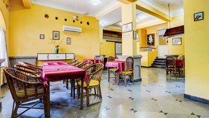 A restaurant with yellow walls, wicker furniture, and tiled flooring. - Super Townhouse Calangute (Calangute)