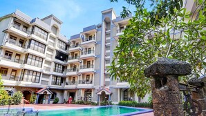 A multi-story hotel with balconies, a swimming pool, and a stone structure. - Super Townhouse Calangute (Calangute)
