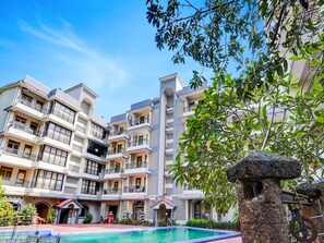 A multi-story hotel with balconies, a swimming pool, and a stone structure. - Super Townhouse Calangute (Calangute)