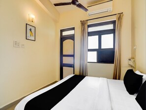 A hotel room with a bed, a ceiling fan, an air conditioning unit, a window with curtains, and a wall-mounted light fixture. - Super Townhouse Calangute (Calangute)