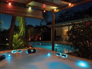 Ein Whirlpool mit integrierter Beleuchtung, umgeben von Palmen und einem Pool.