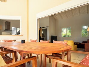 Ein geräumiger Essbereich mit einem großen Holztisch und Bänken, eine Küchenzeile mit Herd und Schränken sowie ein Wohnzimmer mit Sofa und Fernseher.