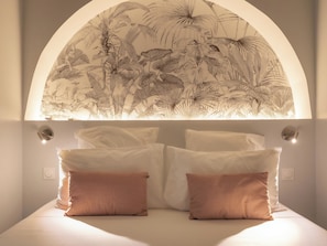 Ein Bett mit zwei Kissen, einer Wandleuchte und einer Decke mit Blattformen.