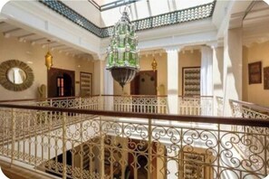 A grand hall with a high ceiling, ornate iron railing, and a central chandelier.