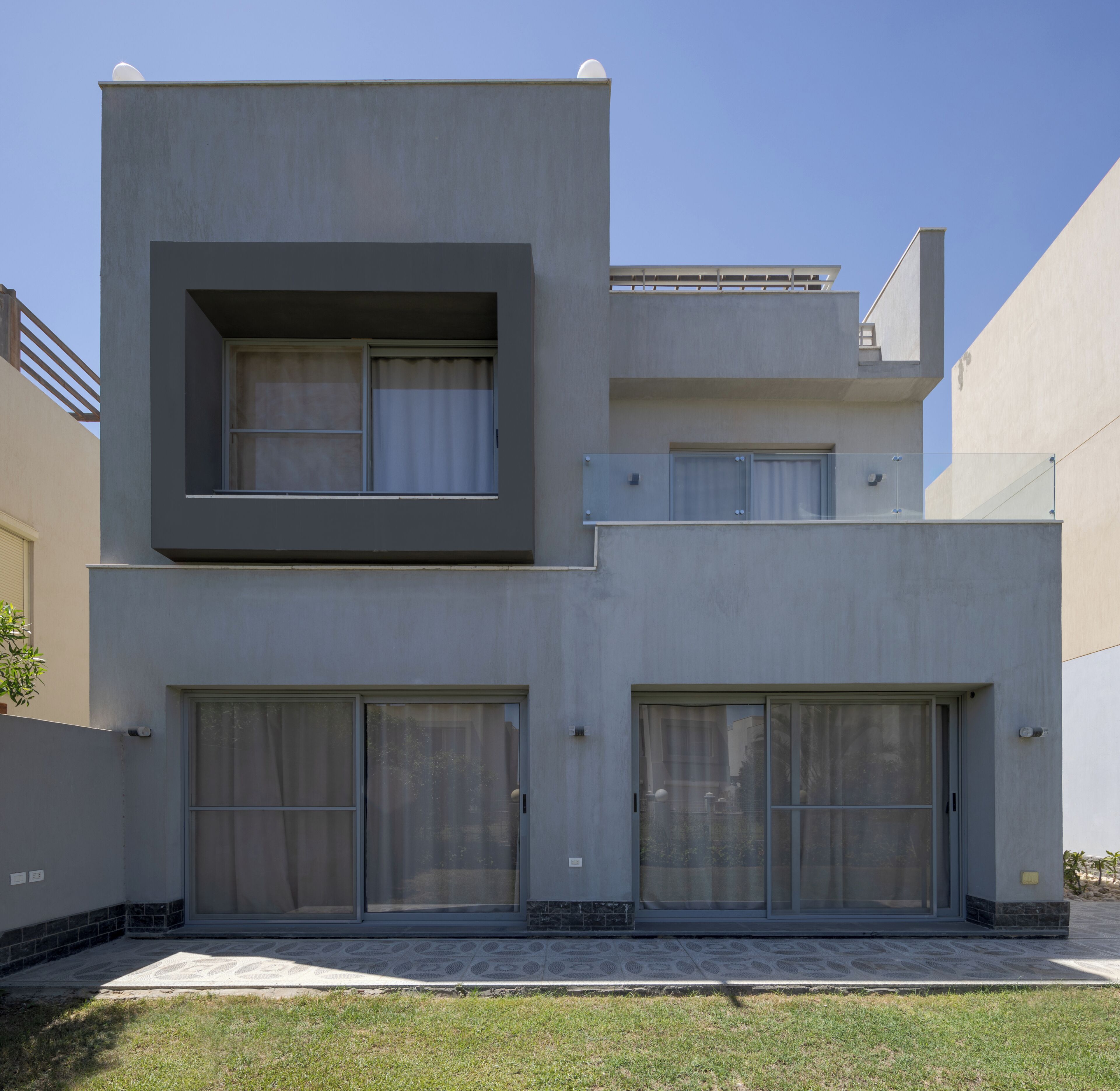 Una moderna casa a due piani con tetto piano, ampie porte scorrevoli in vetro e un piccolo balcone.
