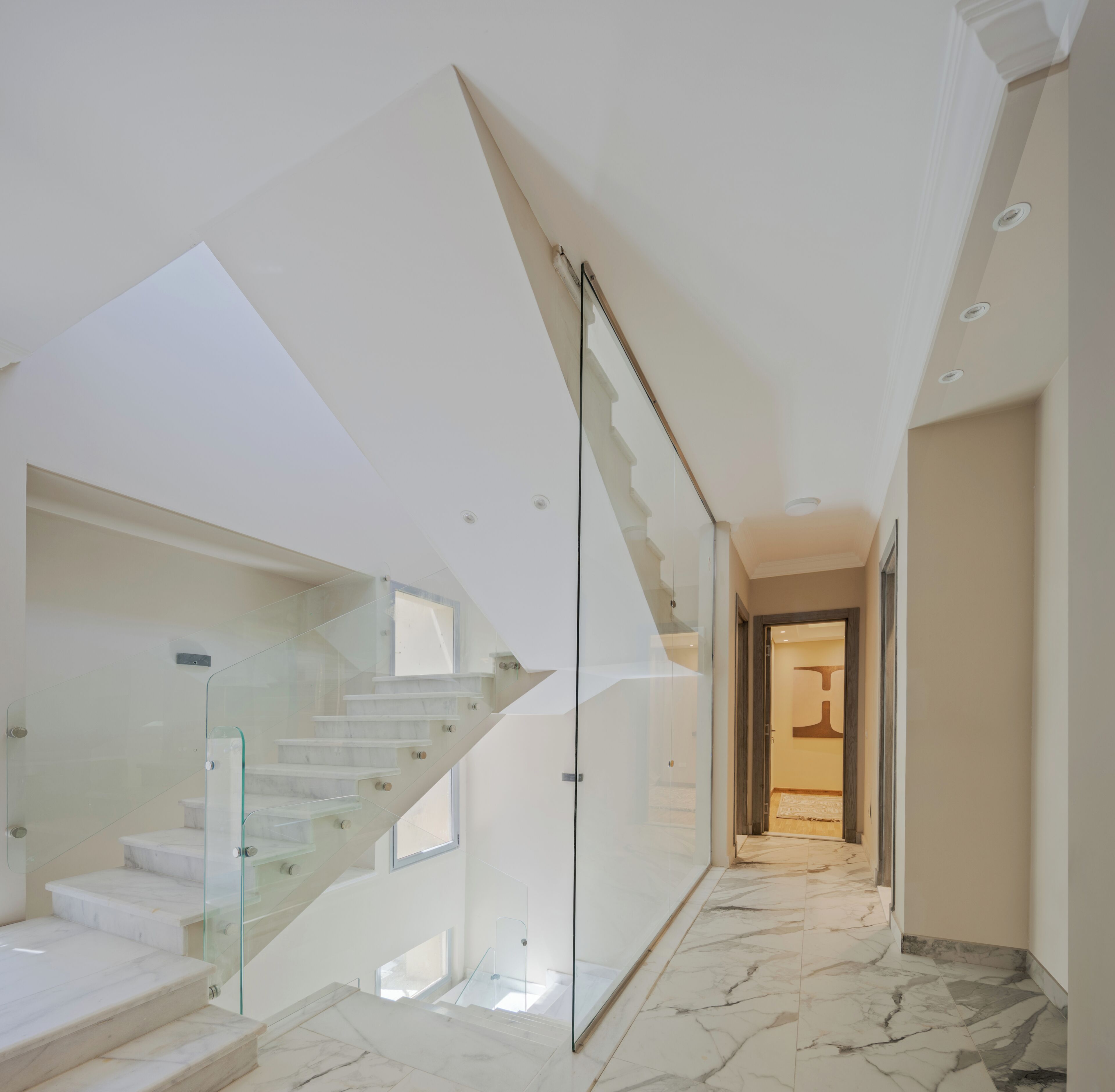 A modern interior with a glass staircase leading to a mezzanine level.