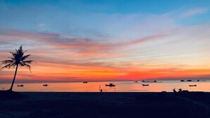 Une scène de plage avec un palmier, des bateaux et un coucher de soleil.