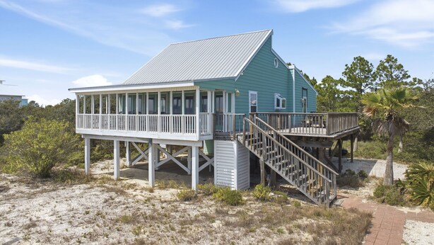 Ein Küstenhaus mit Balkon, einer Treppe und einem Sandstrand im Hintergrund.