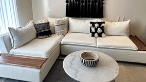 Ein modernes Wohnzimmer mit einem Ecksofa, einem runden Couchtisch und einem dekorativen Wandbild.