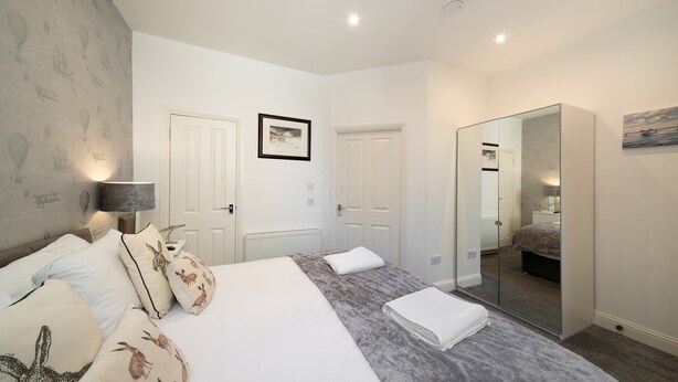 A bedroom with a large bed, two doors, a mirror, and a framed picture on the wall. - Fionas Cottage -  a house that sleeps 6 guests  in 3 bedrooms (Crieff)