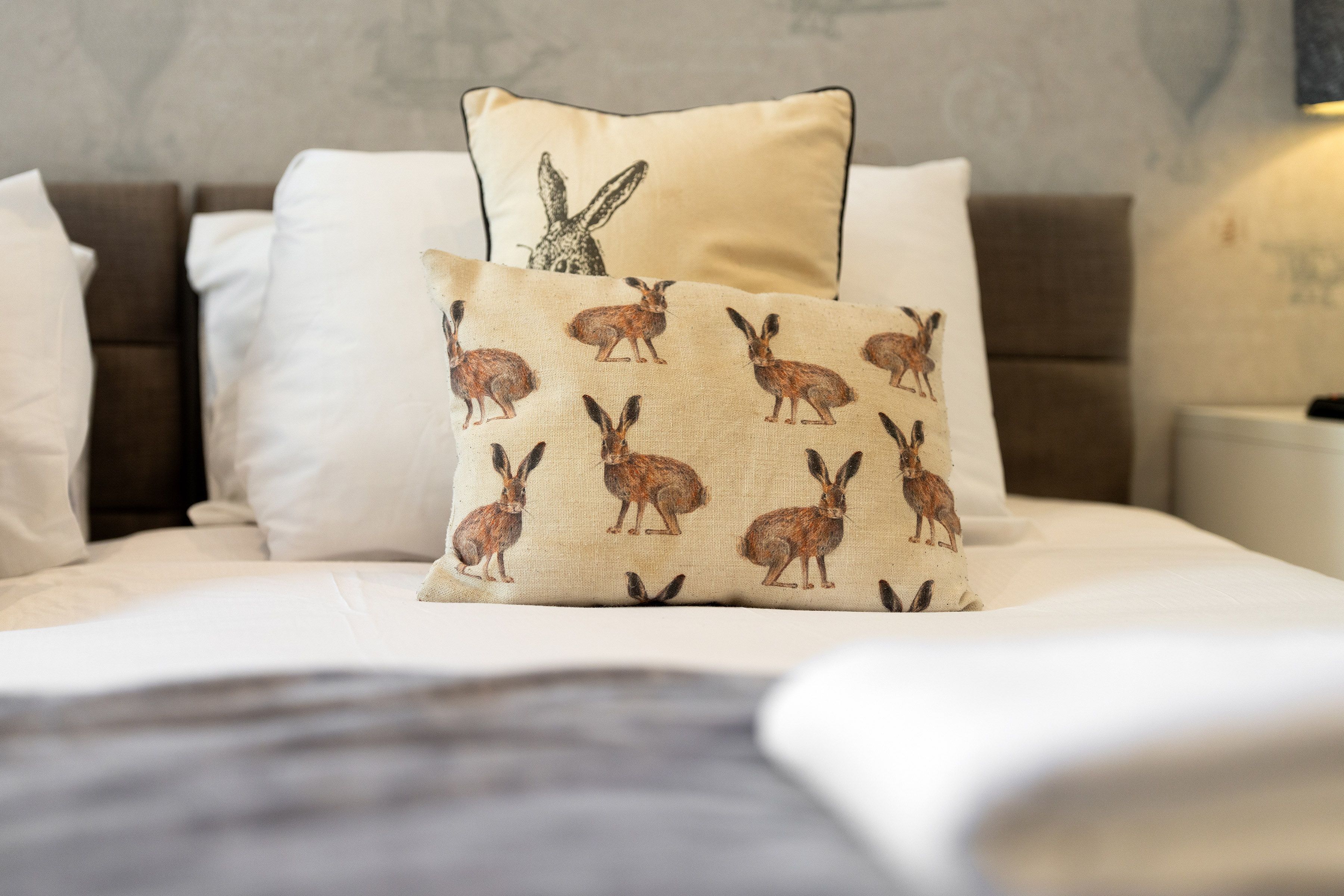 A bed with white bedding, a pillow with a rabbit pattern, and a pillow with a rabbit design.