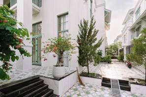 A courtyard with steps leading to a door, surrounded by white buildings with green accents, and a motorcycle parked in the distance. - Regal Villas Tropical Phu Quoc (Phu Quoc)