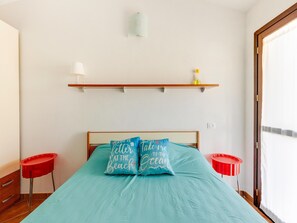A bedroom with a bed, two red side tables, a white wall, a wooden shelf with a bottle, and a window with curtains. - Holiday Home With air Conditioning and Shared Pool (Viddalba)
