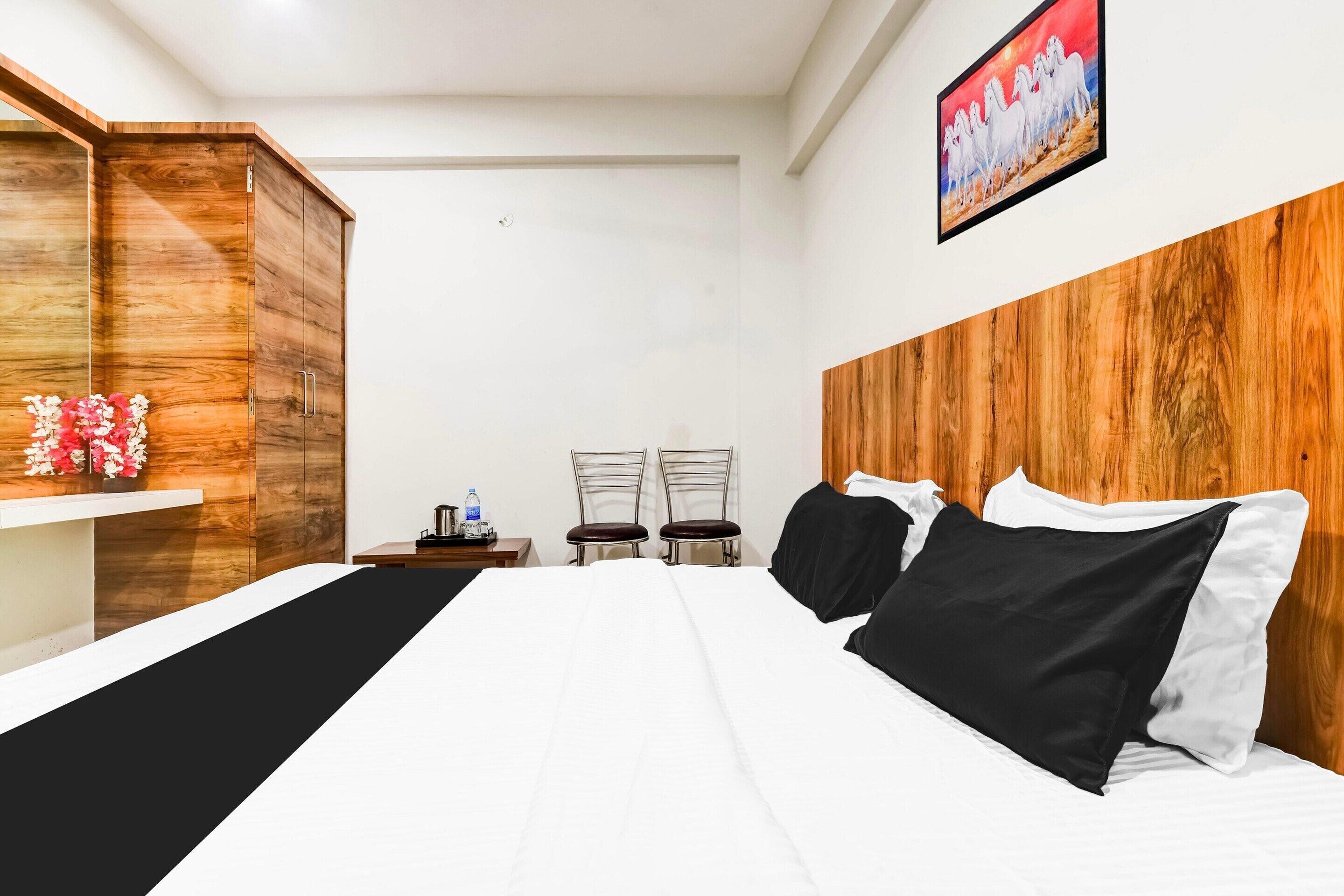 A hotel room with a bed, two chairs, a wooden wardrobe, and a painting on the wall.