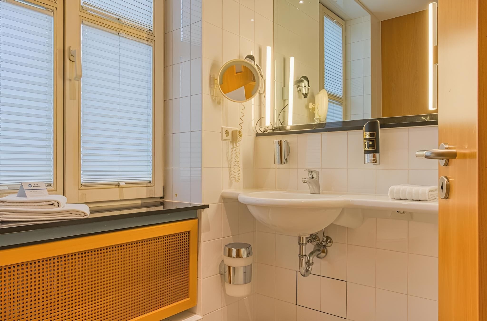 A bathroom with a sink, mirror, towel rack, and window blinds.