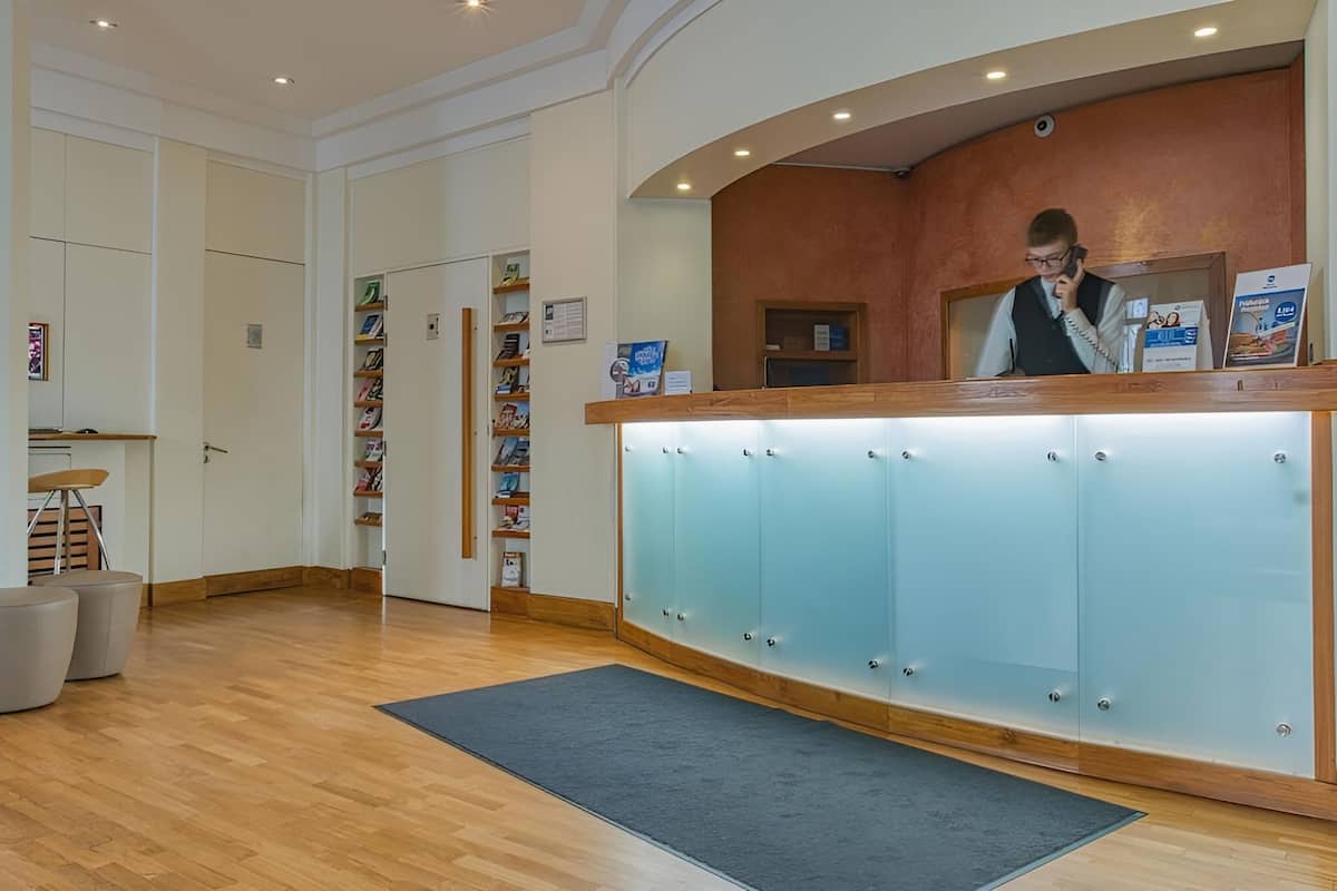 A reception area with a wooden counter, a receptionist, and a wall with framed pictures and a clock.