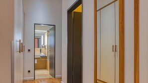 Un couloir avec un plancher en bois, un coin cuisine avec des placards et une armoire avec un miroir.