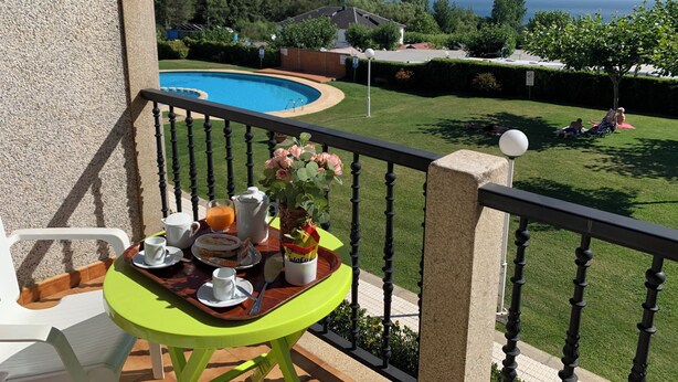 Un balcón con una mesa dispuesta para el desayuno, una piscina y vista al mar.