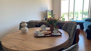 Una mesa de madera redonda con un desayuno sobre una bandeja, un florero con flores y un televisor al fondo.