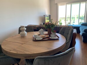 Ein runder Holztisch mit einem Tablett mit Frühstücksgegenständen, einer Blumenvase und einem Fernseher im Hintergrund.