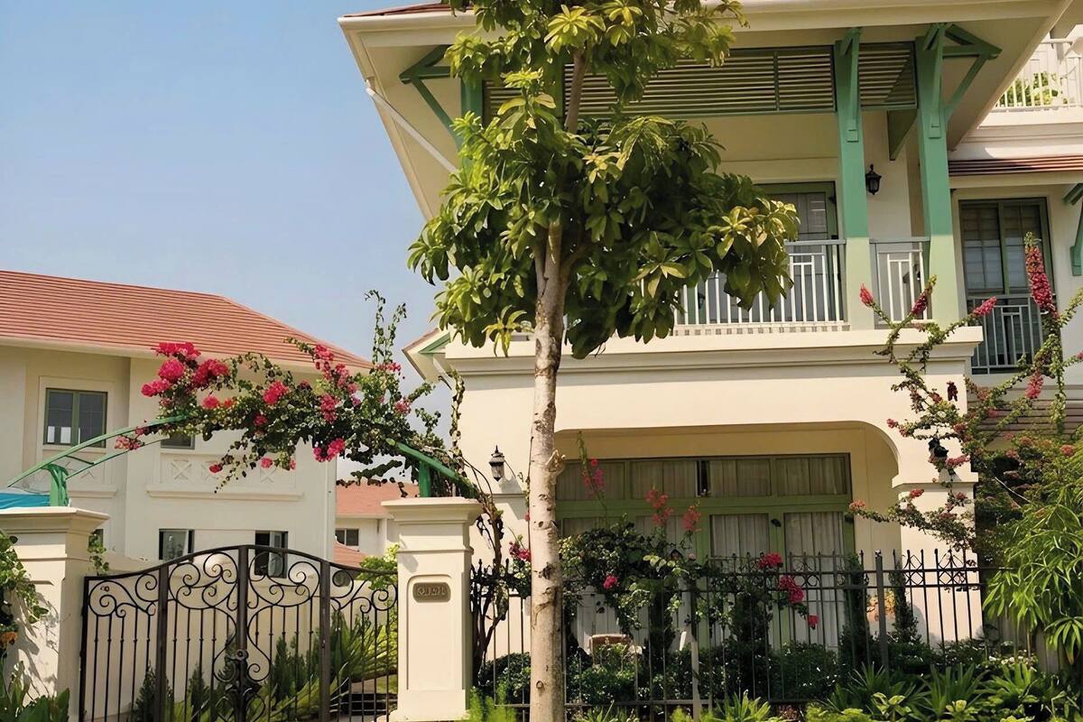 A two-story building with a balcony, surrounded by greenery and a decorative fence.