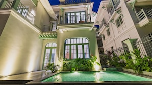 A multi-story building with a swimming pool, balconies, and a gated entrance.
