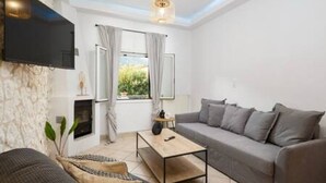 Ett modernt vardagsrum med en soffa, ett soffbord, en platt-TV som är monterad på väggen och ett fönster med gardiner.