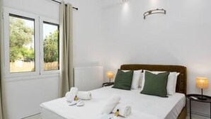 Ett hotellrum med en säng, kuddar, ett sängbord, en lampa och ett fönster med gardiner.