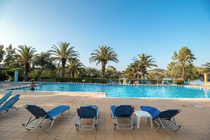 A swimming pool with lounge chairs and palm trees. - Bellu - Govino Bay 2BR Maisonette with Common Pool (Gouvia)