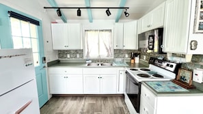 A kitchen with white cabinets, a stove, a sink, and a window with curtains.