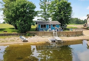 A house by a calm water body with a dock, a boat, and a ladder.