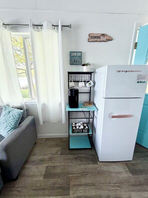 A compact kitchen with a refrigerator, coffee maker, and a coffee bar shelf.