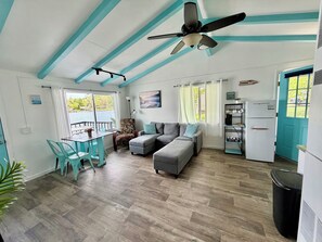 A compact living space with a kitchenette, a dining area with a table and chairs, a sofa, and a ceiling fan.