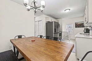 A dining area with a wooden table and chairs, a kitchen with white cabinets, and a staircase leading to another level. - Stylish 4BR Retreat | 2-Car Garage | Sleeps 10 (Omaha)