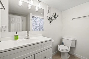A bathroom with a white sink, a toilet, a mirror, and a shower curtain. - Stylish 4BR Retreat | 2-Car Garage | Sleeps 10 (Omaha)