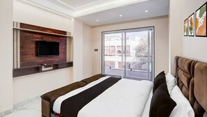 A modern bedroom with a bed, a TV mounted on a wooden panel, a sliding glass door, and a marble floor. - Deluxe Hotel Shree Ganesha (Indore)