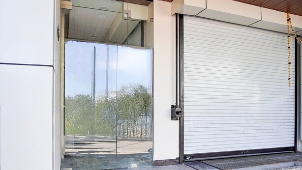 A modern building entrance with a glass door, a metal roller shutter, and a wooden ceiling. - Deluxe Hotel Shree Ganesha (Indore)