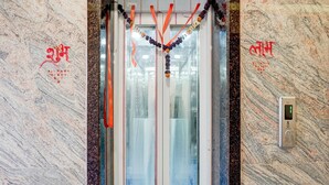 An elevator with a glass door, red and purple garlands, and Hindi text on the wall. - Deluxe Hotel Shree Ganesha (Indore)