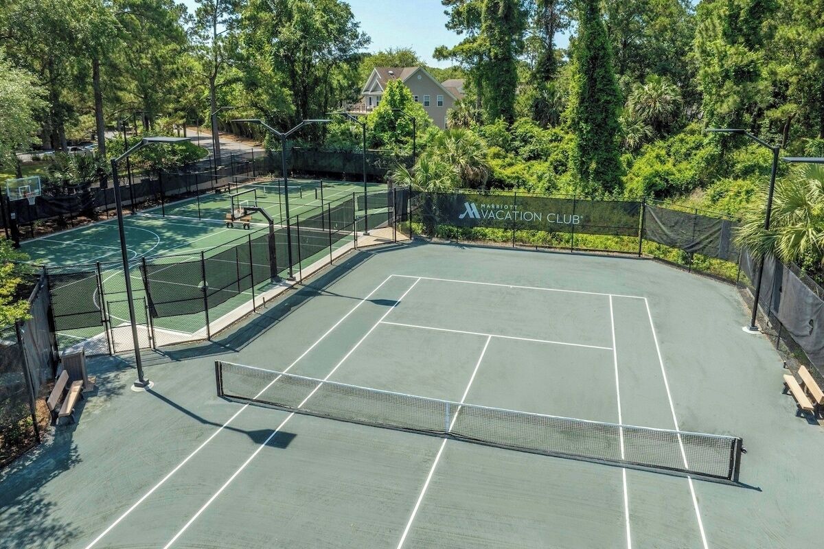 A tennis court with a net, surrounded by trees and a fence.