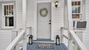 Une maison en bois blanche, avec une porte d’entrée, un paillasson et deux lanternes.