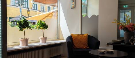 A modern interior with a black sofa, a small round table, potted plants, and a view of the street outside.