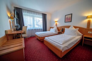 Camera d'albergo con due letti, una scrivania, una sedia, una televisione e una finestra con tende.