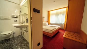 Una habitación de hotel con baño, cama, armario y ventana con cortinas.