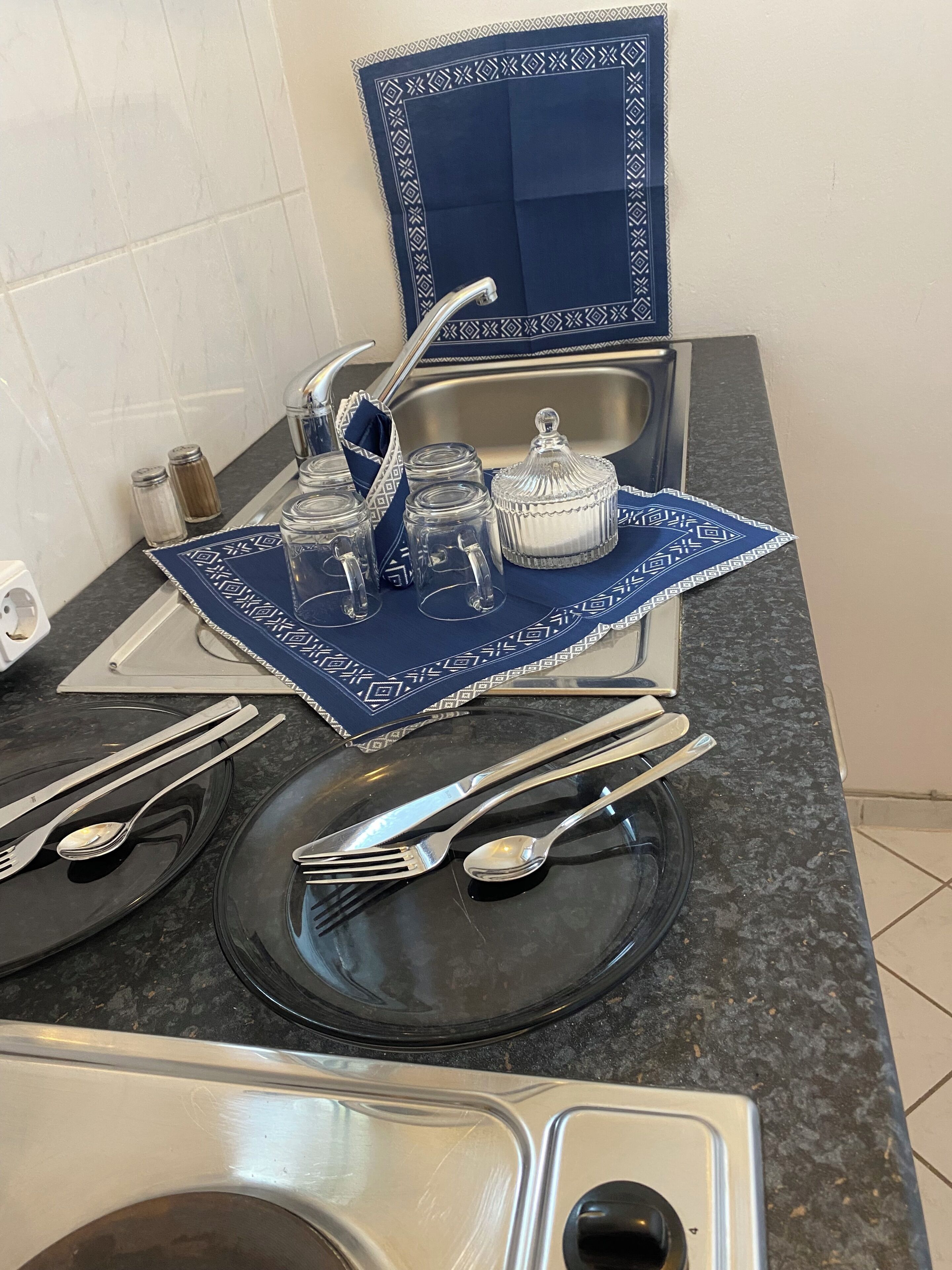 A kitchen counter with a sink, a blue decorative tray with glassware, and a stove.