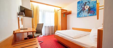 A hotel room with a bed, desk, chair, TV, and artwork on the wall.