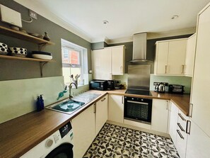A compact kitchen with a dishwasher, oven, and a window with a view. - True Gem” 3-Bed Mews in Westbourne – Steps from Shops & Cafés close to Beach (Bournemouth)