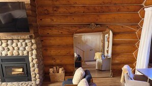 A cozy log cabin interior with a stone fireplace, a sofa set, a round coffee table, and a mirror reflecting the room.
